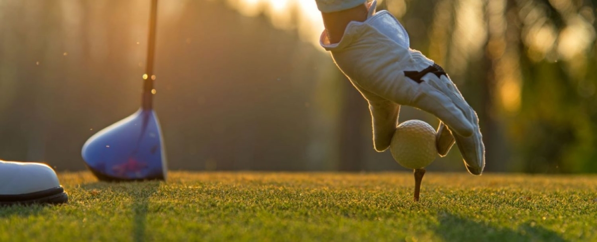 Stock photo of person putting a golf ball on a tee.