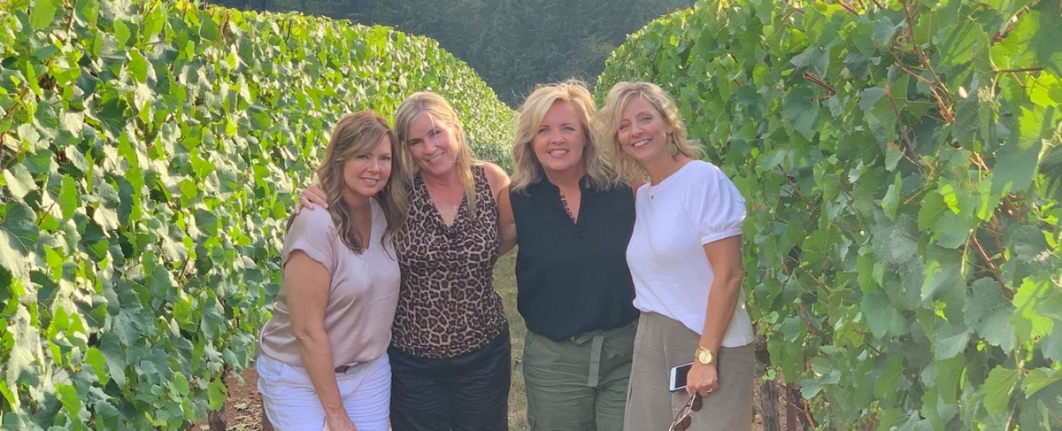 Four women posing in a vineyard field.